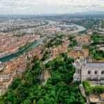 Vue aérienne de Lyon, France, avec la basilique Notre-Dame de Fourvière entourée d'arbres verts, la Saône qui serpente à travers la ville, et des zones urbaines denses - une inspiration parfaite pour toute agence Branding Lyon.