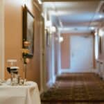 Un couloir d'hôtel avec un éclairage chaleureux et des œuvres d'art encadrées. Au premier plan, une table accueille le dîner du service d'étage - des détails qu'une agence de communication spécialiste hôtellerie en France pourrait mettre en avant pour souligner l'hospitalité exceptionnelle.