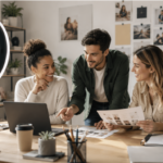 Trois personnes travaillent ensemble à un bureau, entourées d'un ordinateur portable, de documents et d'un café. Les plantes à proximité et une lampe annulaire créent une ambiance particulière, tandis que les créations et les photos accrochées au mur reflètent l'énergie des meilleures agences de communication en France.